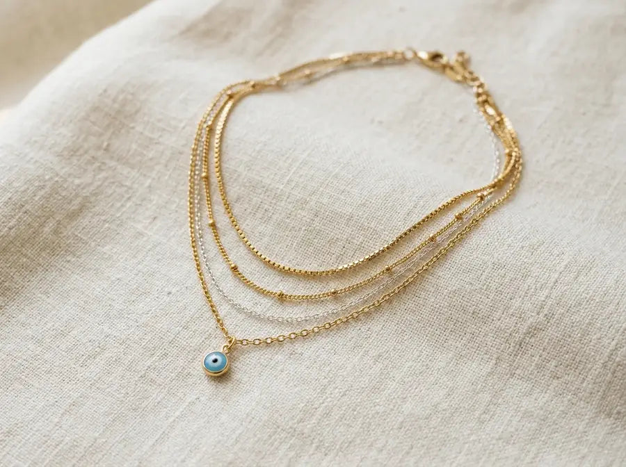 Gold-dominant evil eye stack with one thin silver accent chain as the minority metal tone