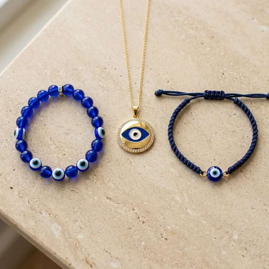 Three evil eye pieces sit side by side: a blue bead bracelet, a gold-tone pendant, and a cord bracelet with the same motif.