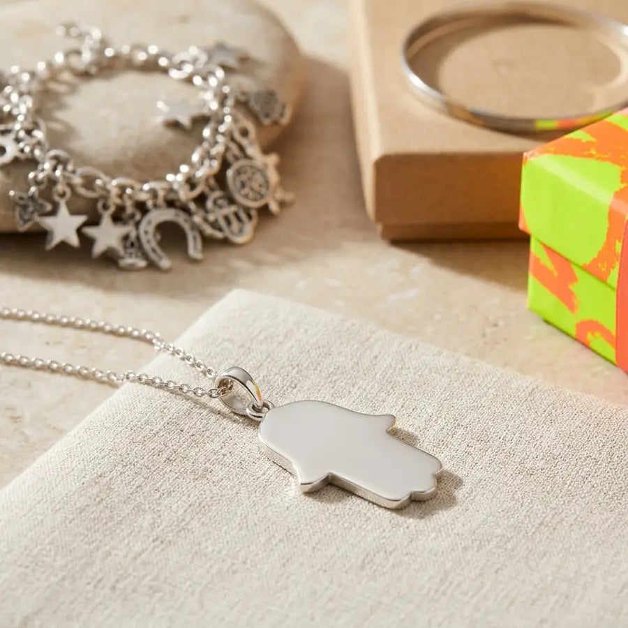 Plain silver Hamsa pendant necklace displayed with a charm bracelet, bangle, and bright gift box.