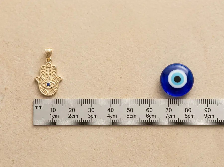 Equal-size Hamsa charm and blue nazar bead aligned horizontally with a slim scale strip between them.