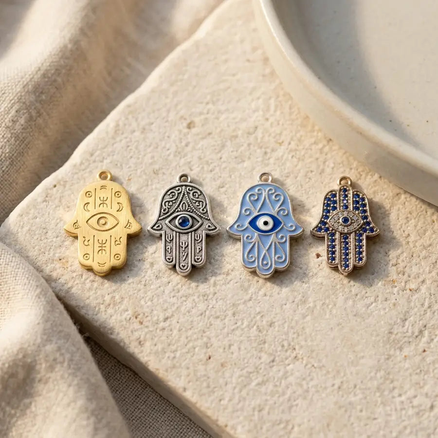 Four Hamsa pieces in a close row showing brushed gold, silver tone, blue enamel, and stone setting details.
