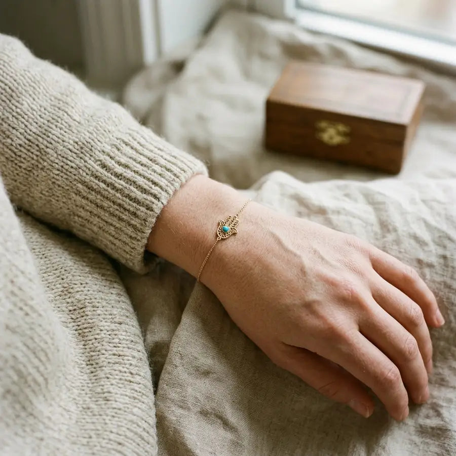 A left wrist held close to the body wearing a centered Hamsa bracelet, with a small blurred keepsake box behind it.