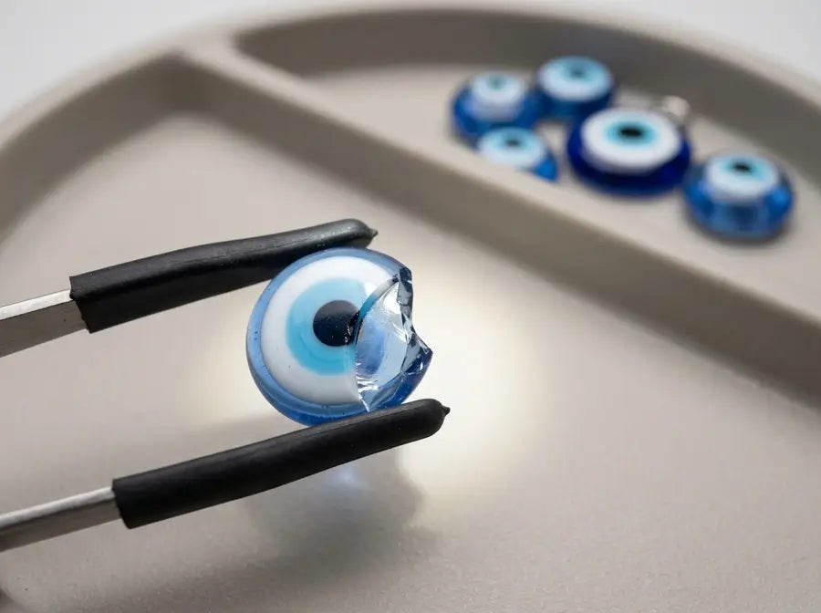 Rubber-tipped tweezers hold a chipped glass bead with a jagged edge while smooth beads and the intact charm remain separated