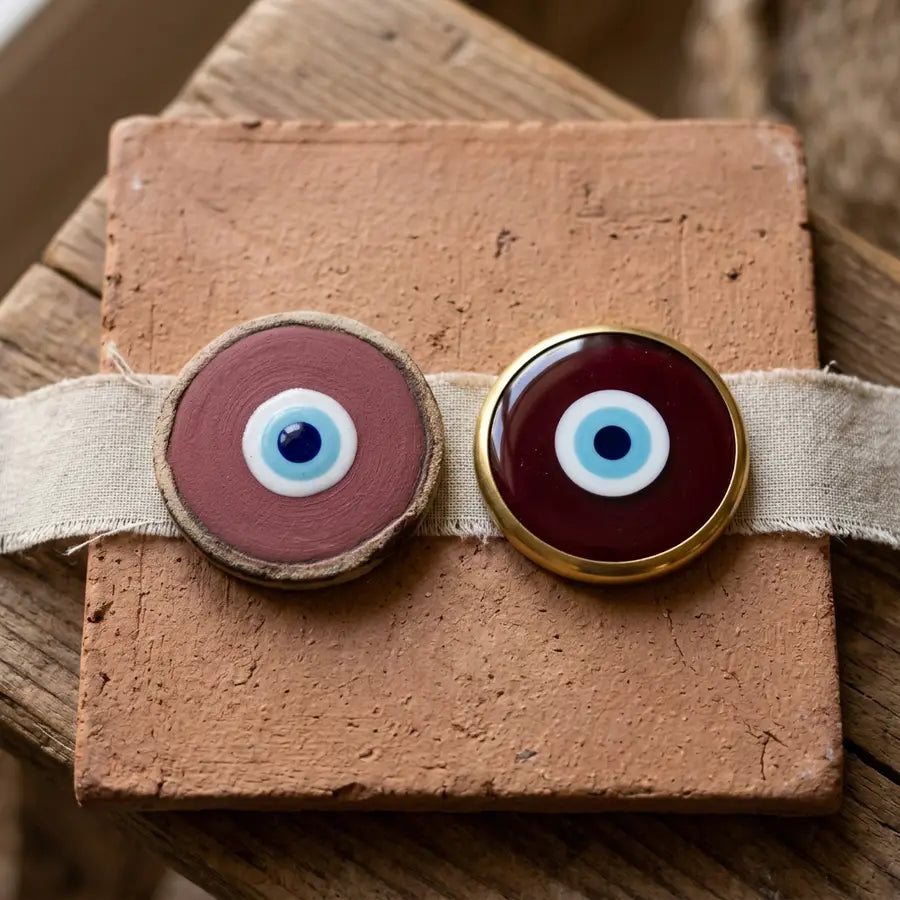 Equal-size matte maroon and polished burgundy evil eye charms side by side on clay tile.