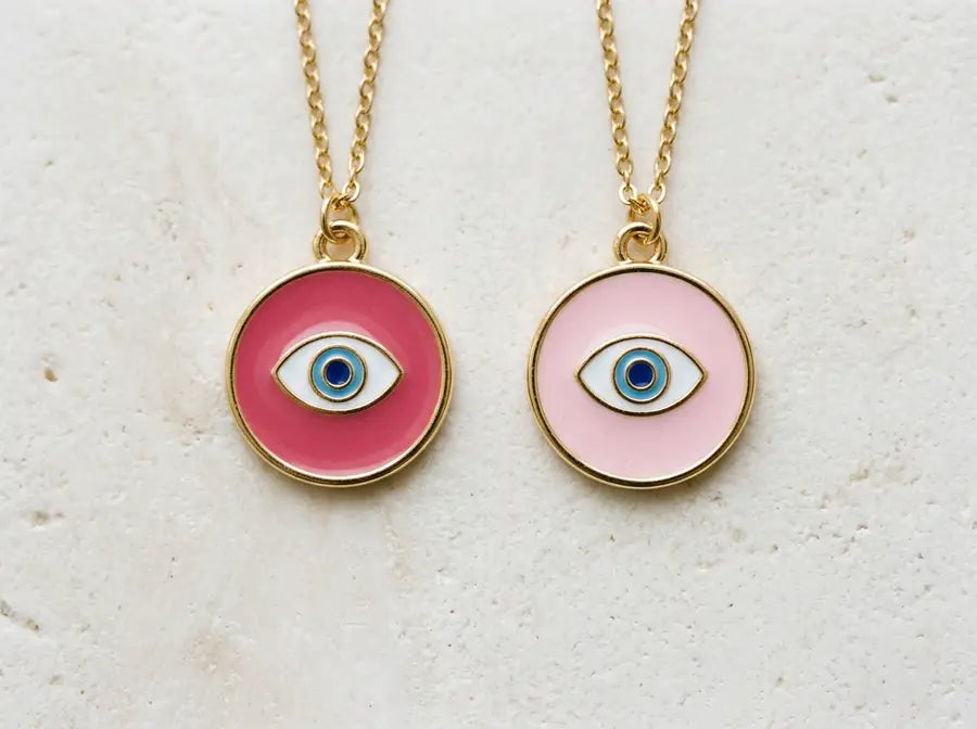 Two matching evil eye charms side by side, one deeper rose pink and one pale light pink