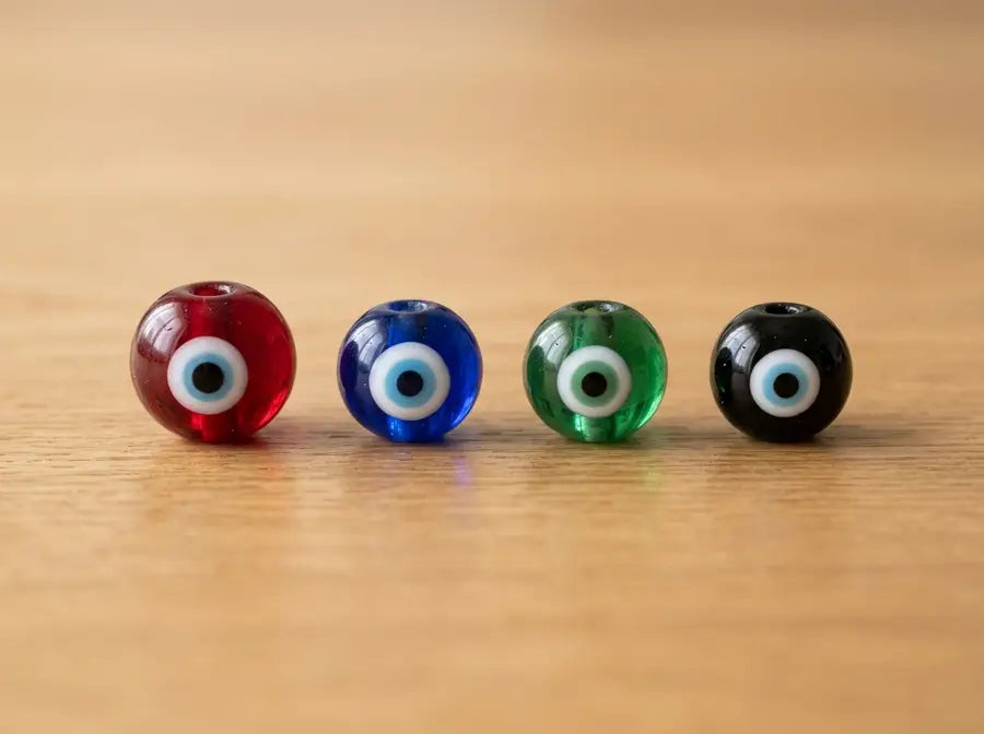 Red, blue, green, and black glass evil eye beads aligned by color on a wooden surface.