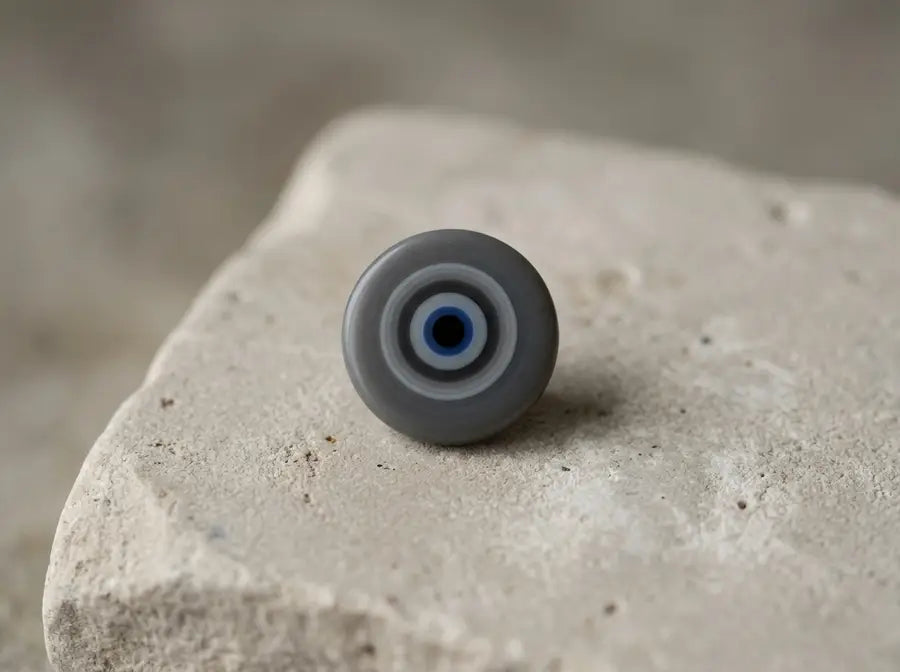 Close view of a grey evil eye charm with concentric charcoal and pale-grey rings; verify against the final visible image.