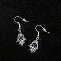 Hamsa hand earrings with blue eyes on a black textured background