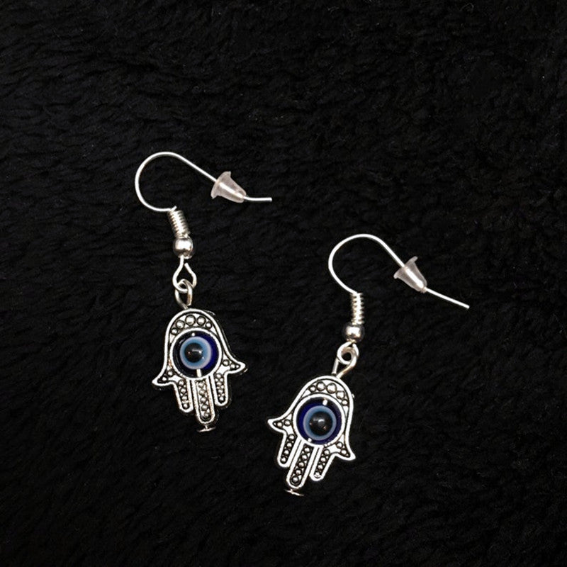 Hamsa hand earrings with blue eyes on a black textured background