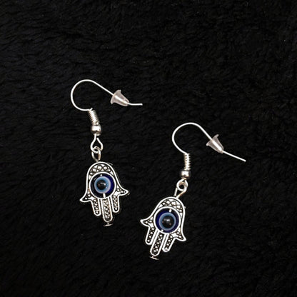 Hamsa hand earrings with blue eyes on a black textured background
