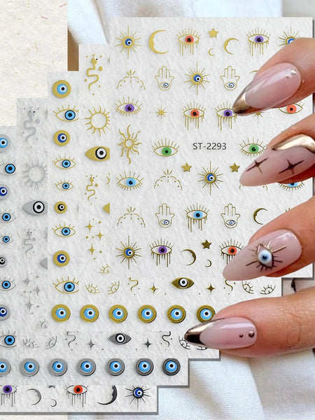 Nail art sticker sheets with various eye, crescent moon, and hamsa designs, held by a hand with manicured nails against a light fabric background.