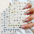 Nail art sticker sheets with various eye, crescent moon, and hamsa designs, held by a hand with manicured nails against a light fabric background.