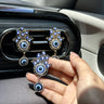 Silver tone Hamsa vent clip held in a hand, showing its blue eye details and pendant in front of two gold tone clips.