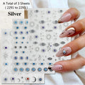 Three sheets of silver nail art stickers featuring evil eye, sun, moon, and star designs, held by a hand with manicured nails decorated with matching eye designs.