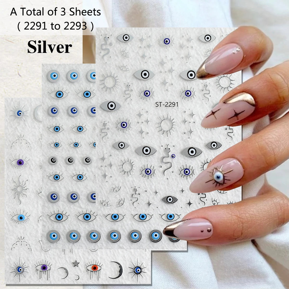 Three sheets of silver nail art stickers featuring evil eye, sun, moon, and star designs, held by a hand with manicured nails decorated with matching eye designs.