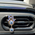 One gold tone Hamsa car vent clip with blue eye motifs, clear accents and a round hanging eye pendant.