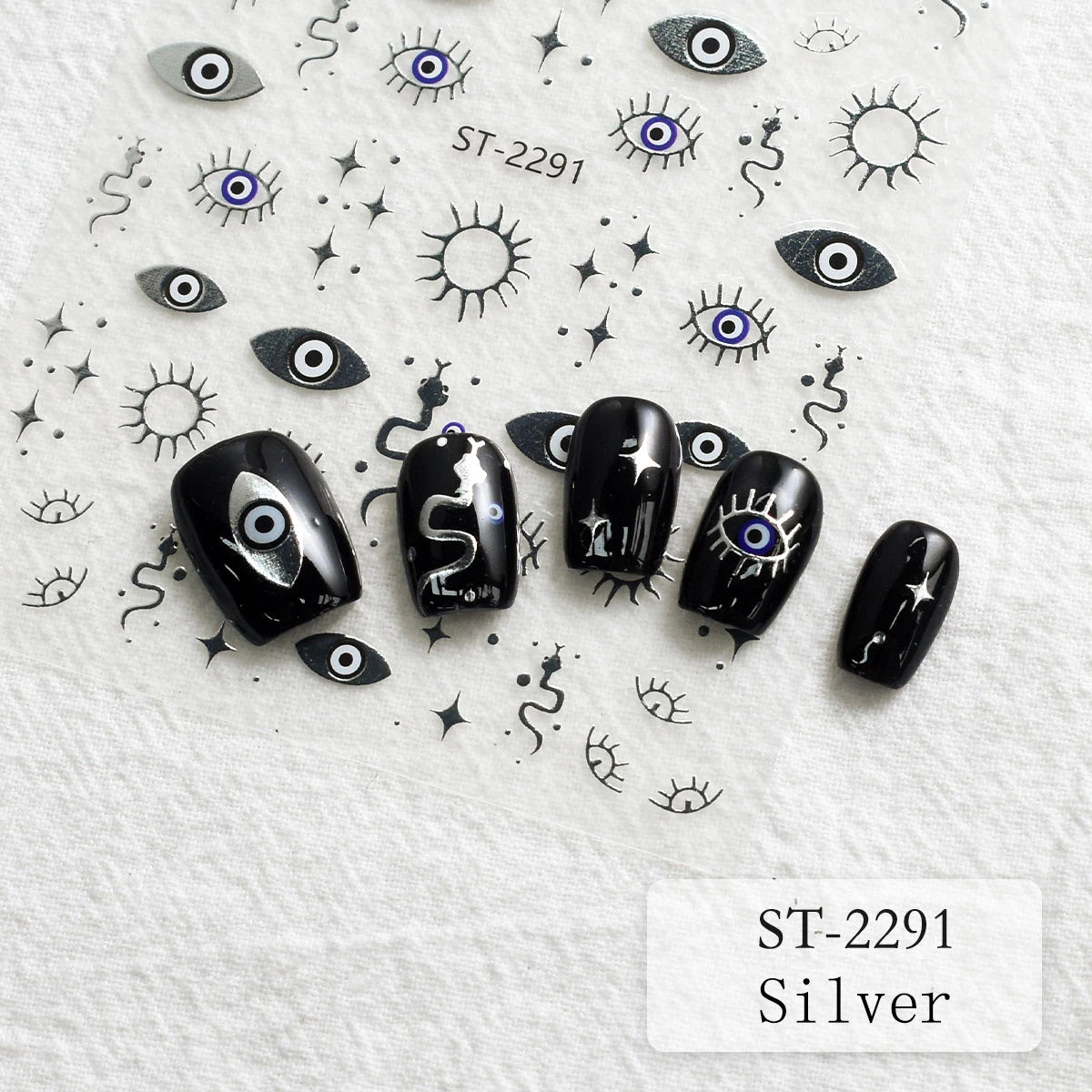 Five black nail art decals or false nail tips with silver and blue evil eye designs are arranged on a white textured background, surrounded by matching small eye, star, and wavy line motifs. Text reads ST-2291 and Silver.