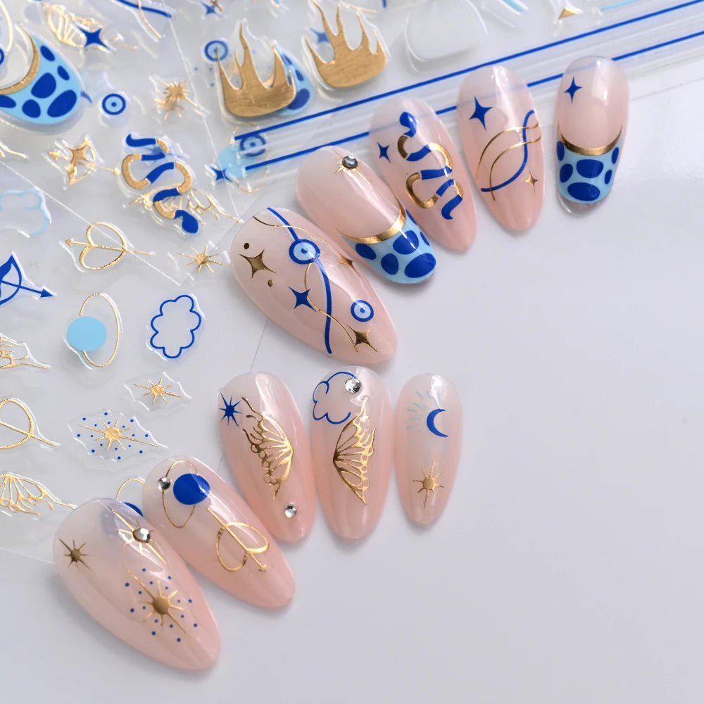 Blue and gold-tone nail sticker manicures with evil eye, moon, star, and shell motifs