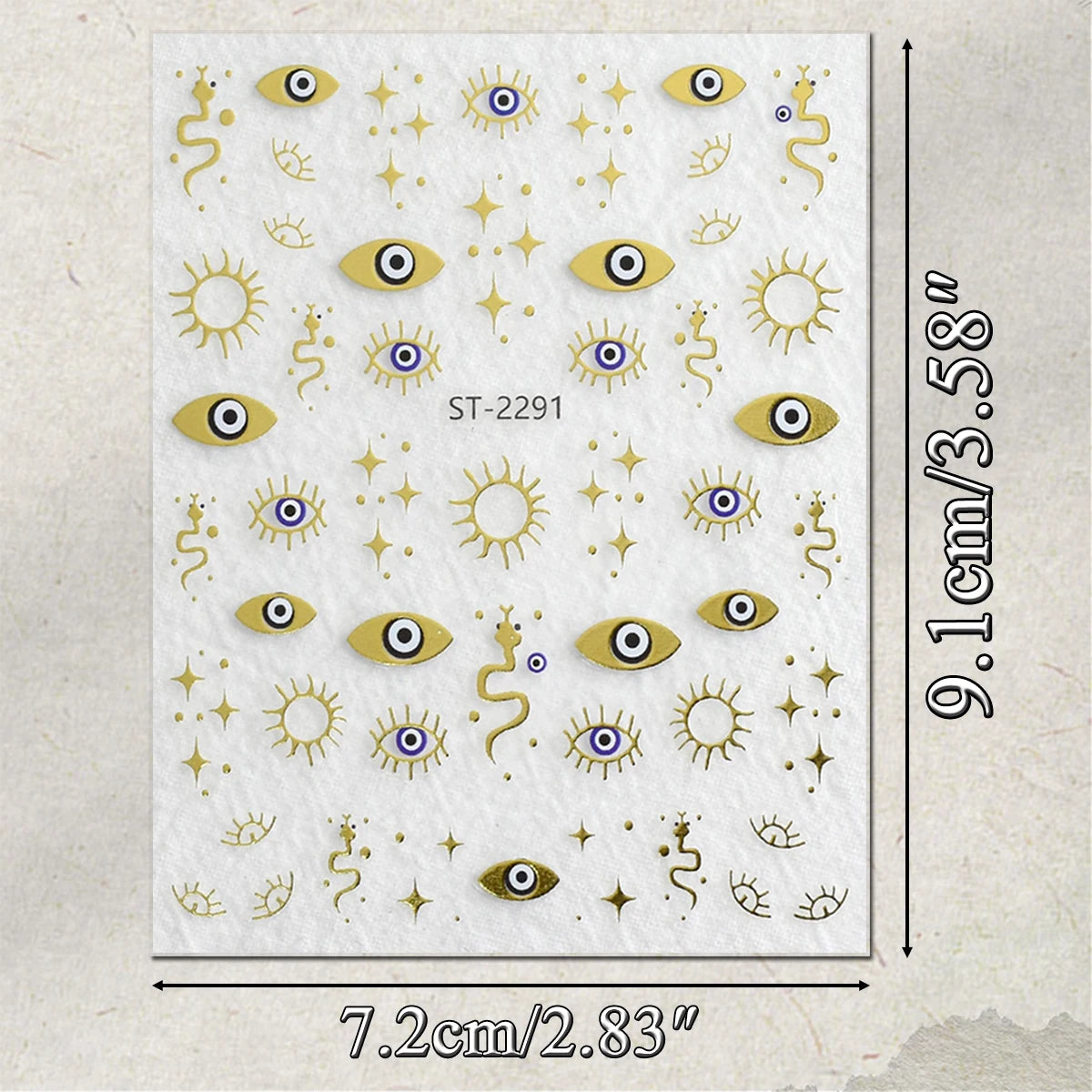 A sheet of decorative stickers featuring gold-toned suns, stars, evil eye motifs, and snake illustrations on a white background, with printed dimensions showing 9.1 cm by 7.