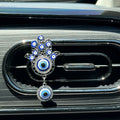 One silver tone Hamsa car vent clip with blue eye motifs, clear accents and a round hanging eye pendant.