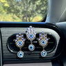 Two gold tone and one silver tone Hamsa clips displayed on a car vent, each with blue eyes and a round hanging pendant.