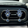 Front view of two silver tone Hamsa clips on a dark car vent, showing open hand outlines and clear accents around the blue eyes.