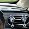 Two silver tone Hamsa clips with round blue eye pendants on a car vent, viewed at an angle with the surrounding dashboard visible.