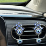 Two silver tone Hamsa clips with round blue eye pendants on a car vent, viewed at an angle with the surrounding dashboard visible.
