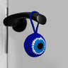 Blue round evil eye charm hanging from a black door handle, viewed at an angle showing its rounded edge.