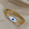 Gold tone evil eye bangle angled upward to the left, showing the clear accent border and rectangular band pattern