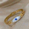 Gold tone evil eye bangle angled upward to the right, with a white eye and raised blue center