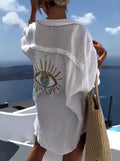 Back view of a white shirt with a large sequin eye motif, crinkled texture and curved hem