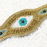 Close-up of a turquoise, white and black beaded eye surrounded by gold tone beads and chain edging.