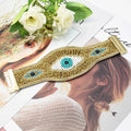 Gold tone beaded cuff bracelet laid across a magazine beside white flowers, with all three eye motifs visible.