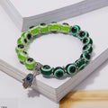 Bracelet with light and dark green eye beads, silver tone spacers and a dangling Hamsa hand with a blue eye, resting on an open book.
