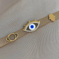 Gold tone mesh bracelet laid flat with a blue and white eyelash eye, a smaller open eye motif, and a scalloped accent