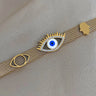 Gold tone mesh bracelet laid flat with a blue and white eyelash eye, a smaller open eye motif, and a scalloped accent