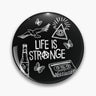 Black round button pin with Life Is Strange lettering, a triangular eye, bird, butterflies and cassette in white.