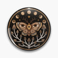 Black round button pin with a brown moth bearing eye motifs, moon phases, stars and branching mushrooms.