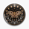 Black round button pin with a brown moth bearing eye motifs, moon phases, stars and branching mushrooms.