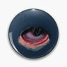 Round dark blue button pin with a painterly eye in black, purple, pink and orange.