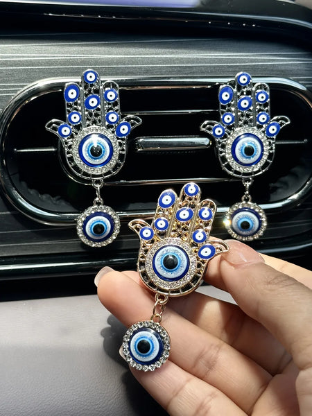 Gold tone Hamsa vent clip held in a hand, with two silver tone clips displayed on the vent behind it.