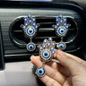 Gold tone Hamsa vent clip held in a hand, with two silver tone clips displayed on the vent behind it.