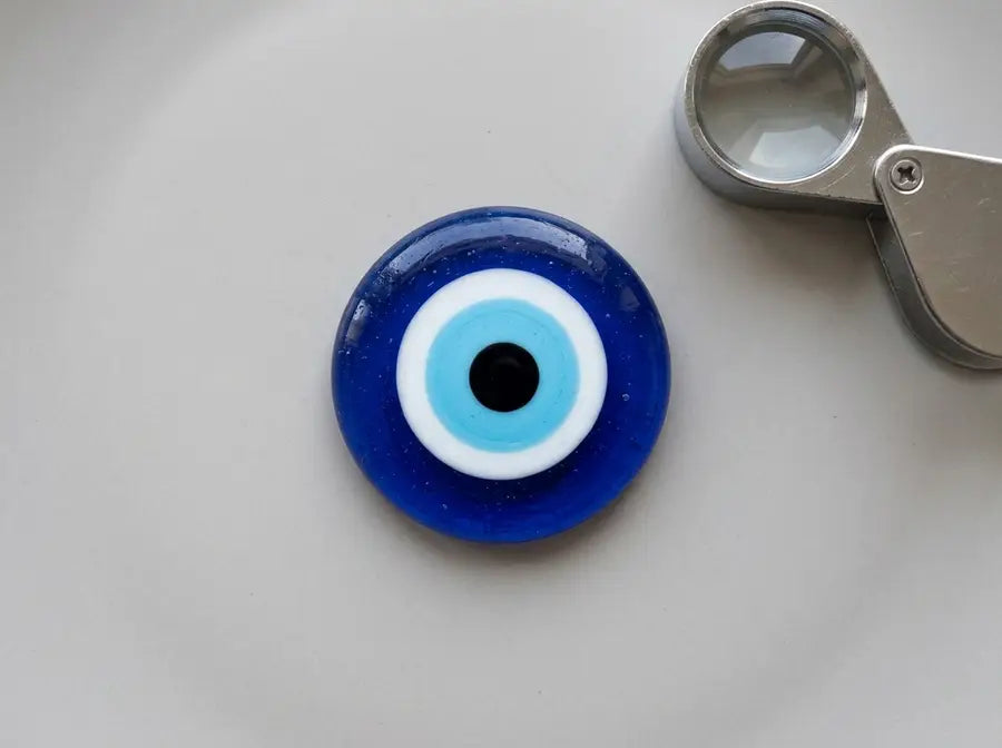 Overhead macro revealing a dark-blue outer disk, white ring, light-blue iris, and black pupil beside a clear jeweler's loupe.