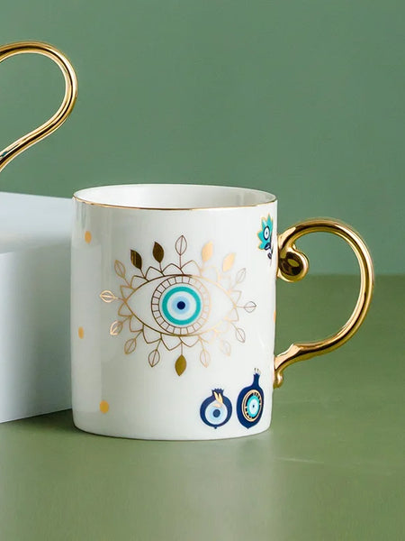 White coffee cup with a turquoise eye, gold tone leaf border and curved gold tone handle.