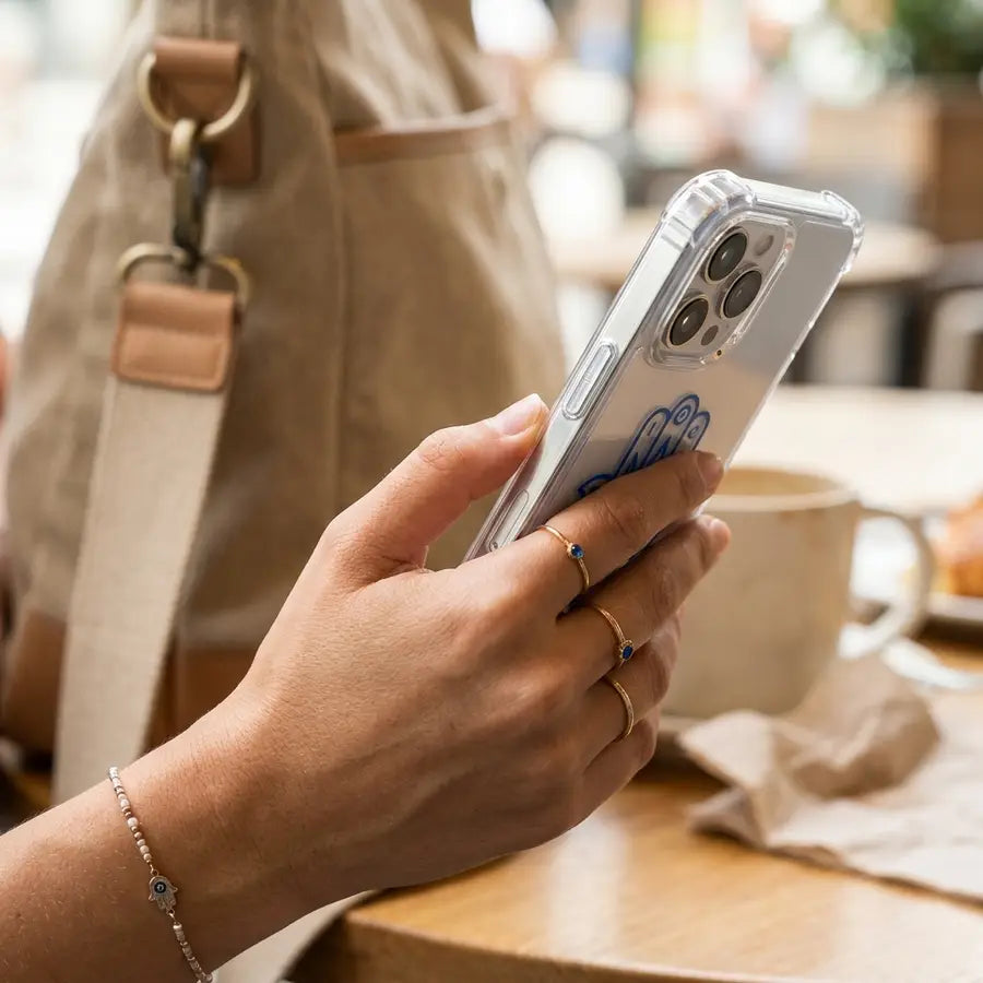 Hand gripping a clear Hamsa evil eye phone case with visible raised camera lip, corner coverage, side buttons, and raised edg