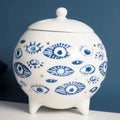 White footed jar with a domed lid, varied blue eye motifs and gold tone dots