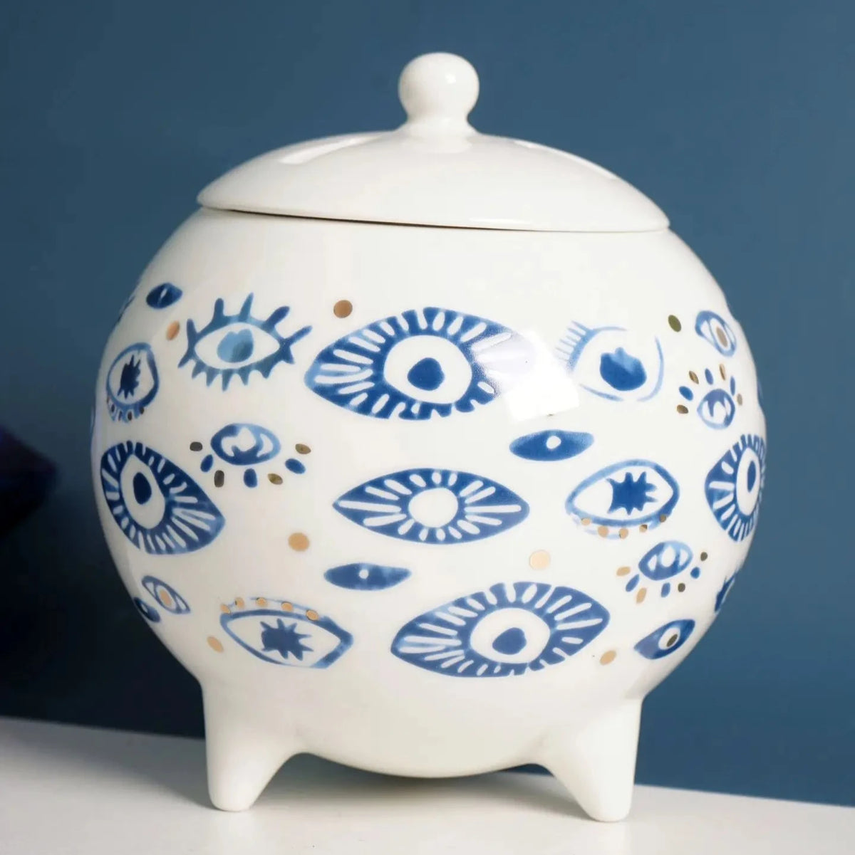 White footed jar with a domed lid, varied blue eye motifs and gold tone dots