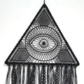 Close-up of the black triangular dream catcher showing its central eye, radiating lines, mesh corners and patterned fringe.