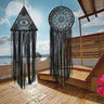 Black triangular eye and round floral dream catchers hanging side by side in a terrace setting overlooking water.